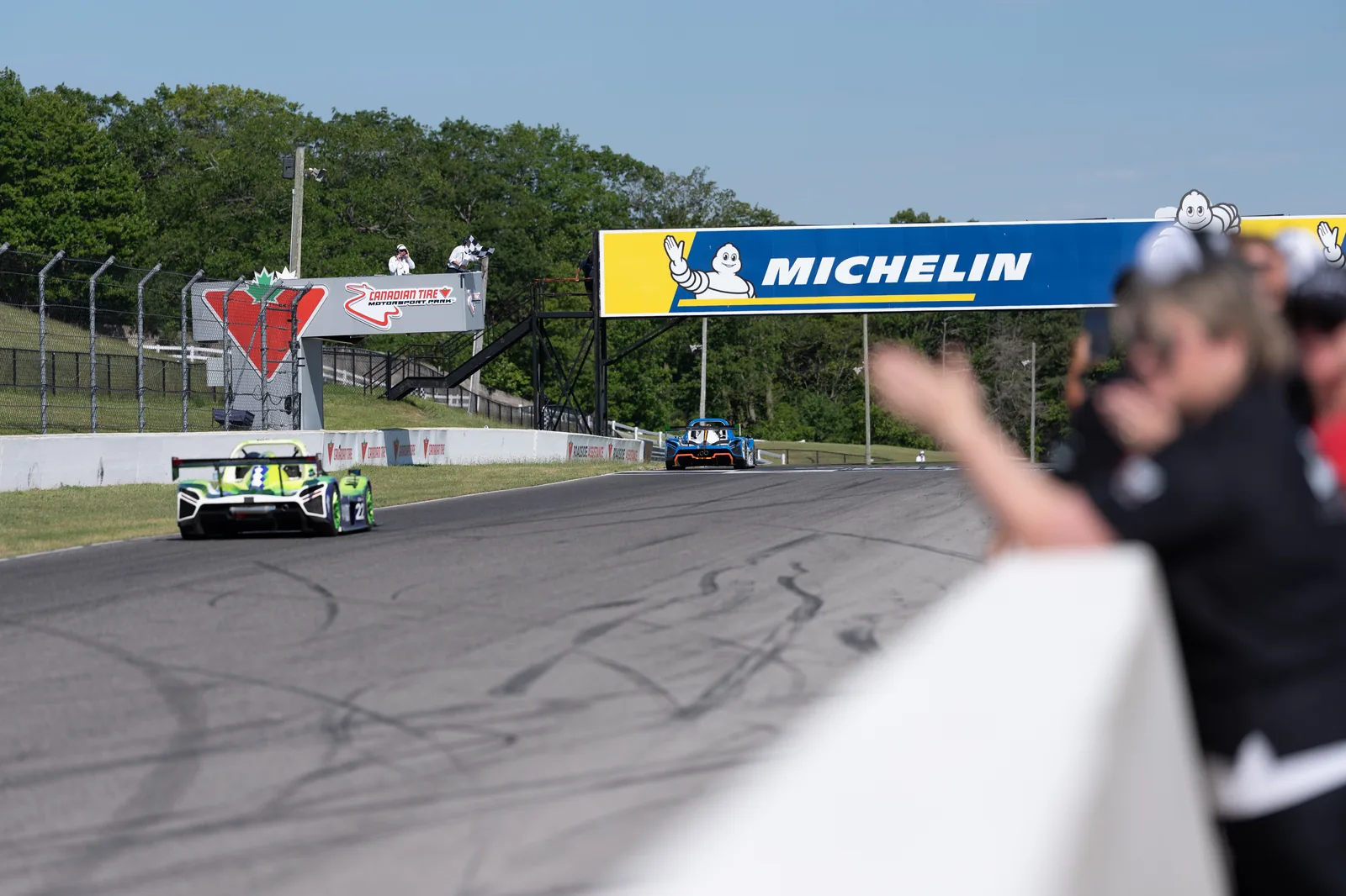 Radical race cars crossing the finish line under the checkered flag at Canadian Tire Motorsport Park with the Michelin bridge behind
