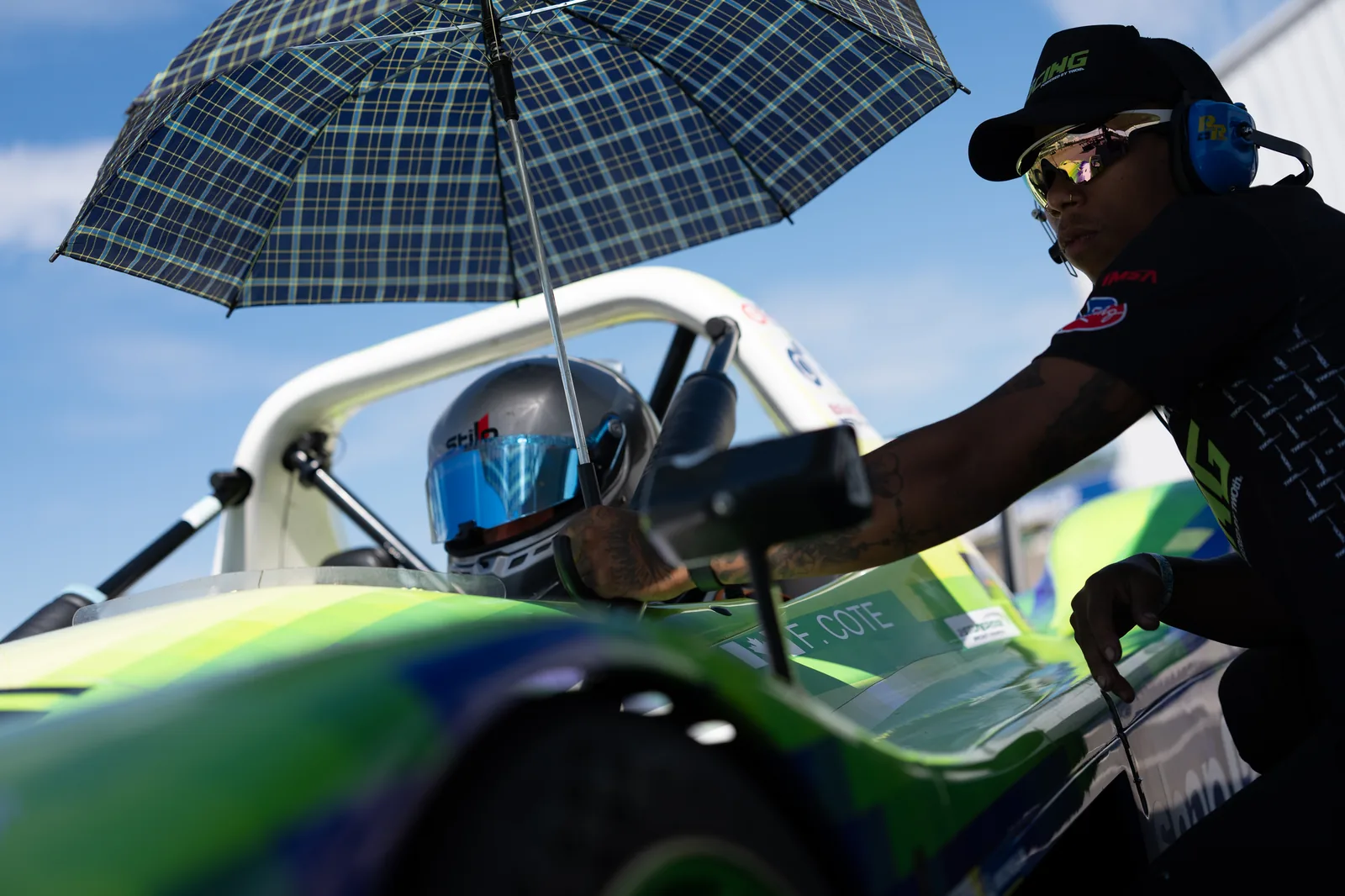Francois Cote sitting in the Radical SR3 on the grid at Canadian Tire Motorsport Park while a TWOth crew member holds an umbrella over the cockpit