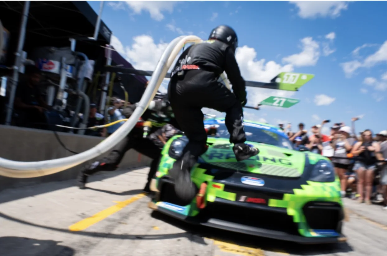 A TWOth crew member leaping over the green number 22 Shopify Racing Porsche during a pit stop at CTMP